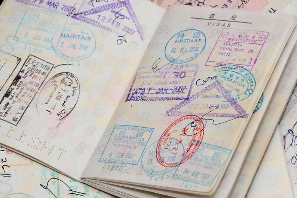 Ein aufgeschlagener Ausweis zeigt Seiten, die mit bunten Ein- und Ausreisestempeln, Visa und handschriftlichen Notizen gefüllt sind - jeder Eintrag steht für eine ausgedehnte internationale Reise durch viele Länder. | adelstitel-kaufen.com