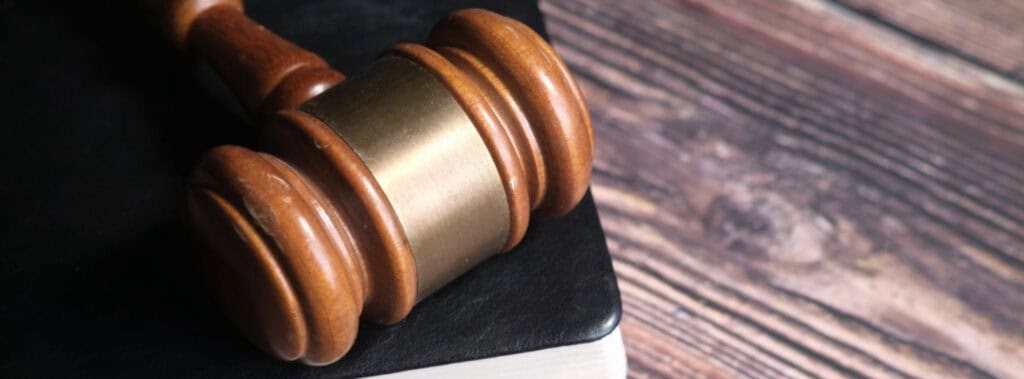 Auf einem Holztisch liegt ein hölzerner Richterhammer auf einem geschlossenen schwarzen Buch, das an die Feierlichkeit der Justiz nach dem deutschen Grundgesetz erinnert. | adelstitel-kaufen.com